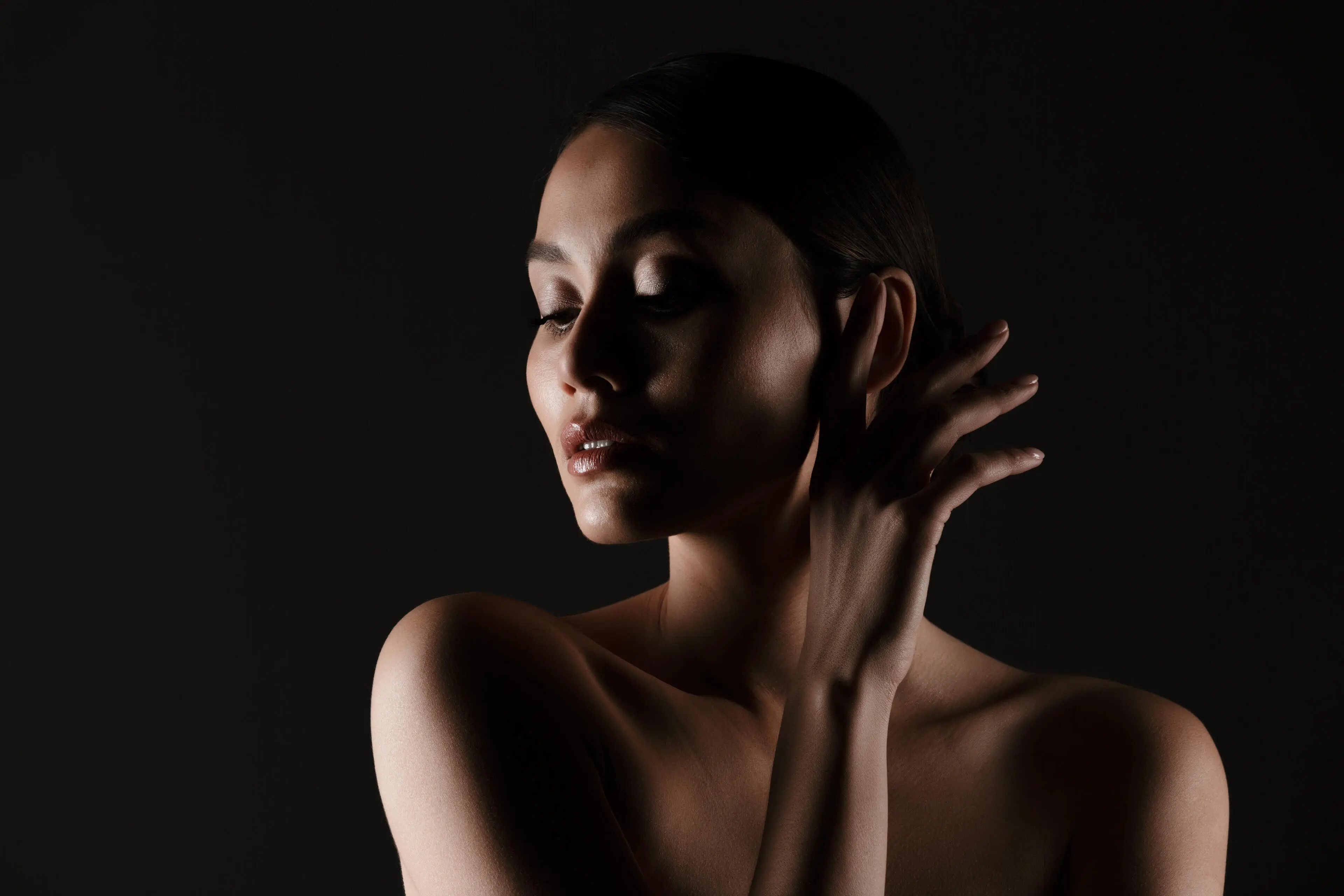 Portrait feminine tender woman with sensual look looking aside low lights isolated black
