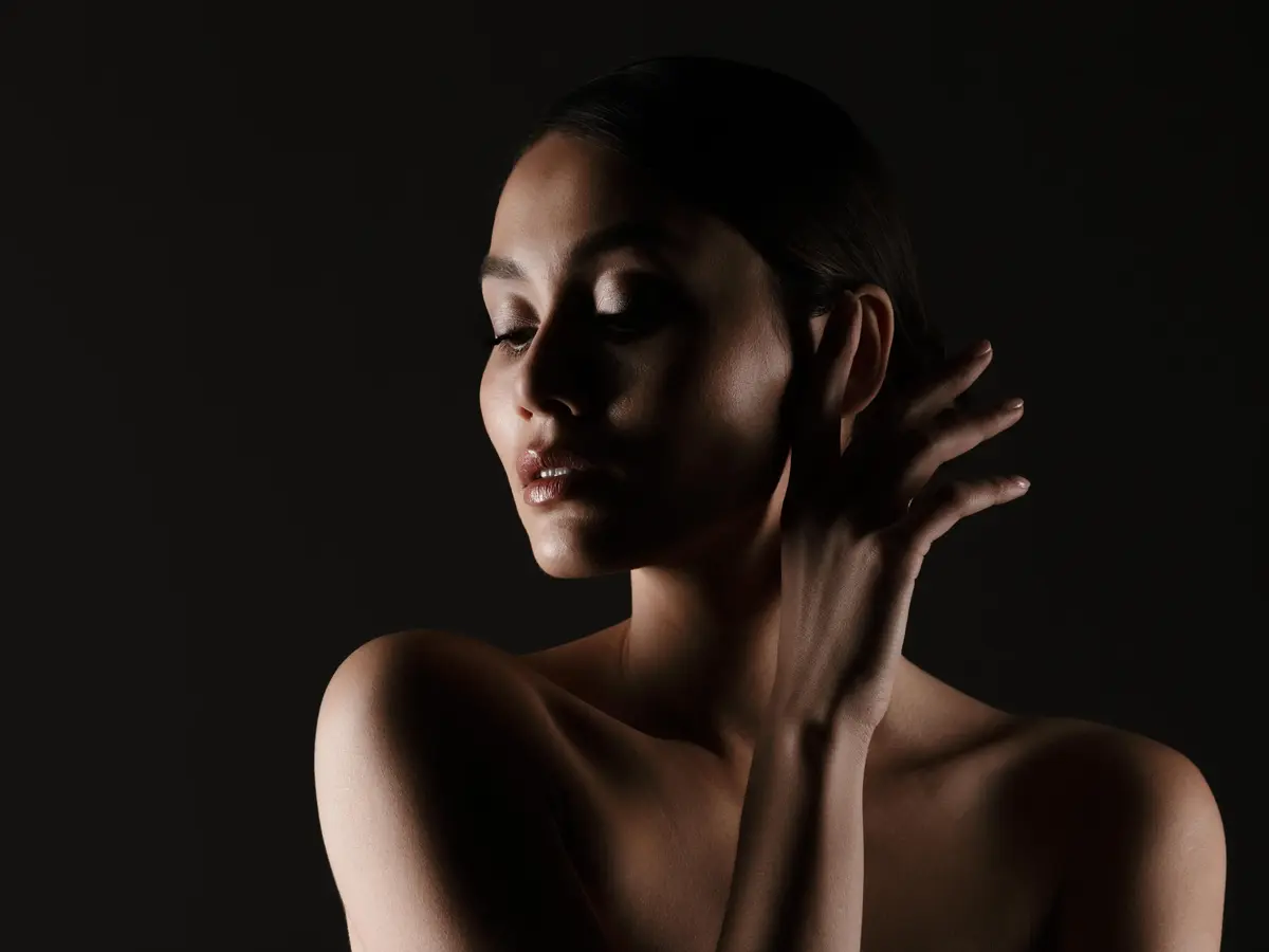 Portrait feminine tender woman with sensual look looking aside low lights isolated black