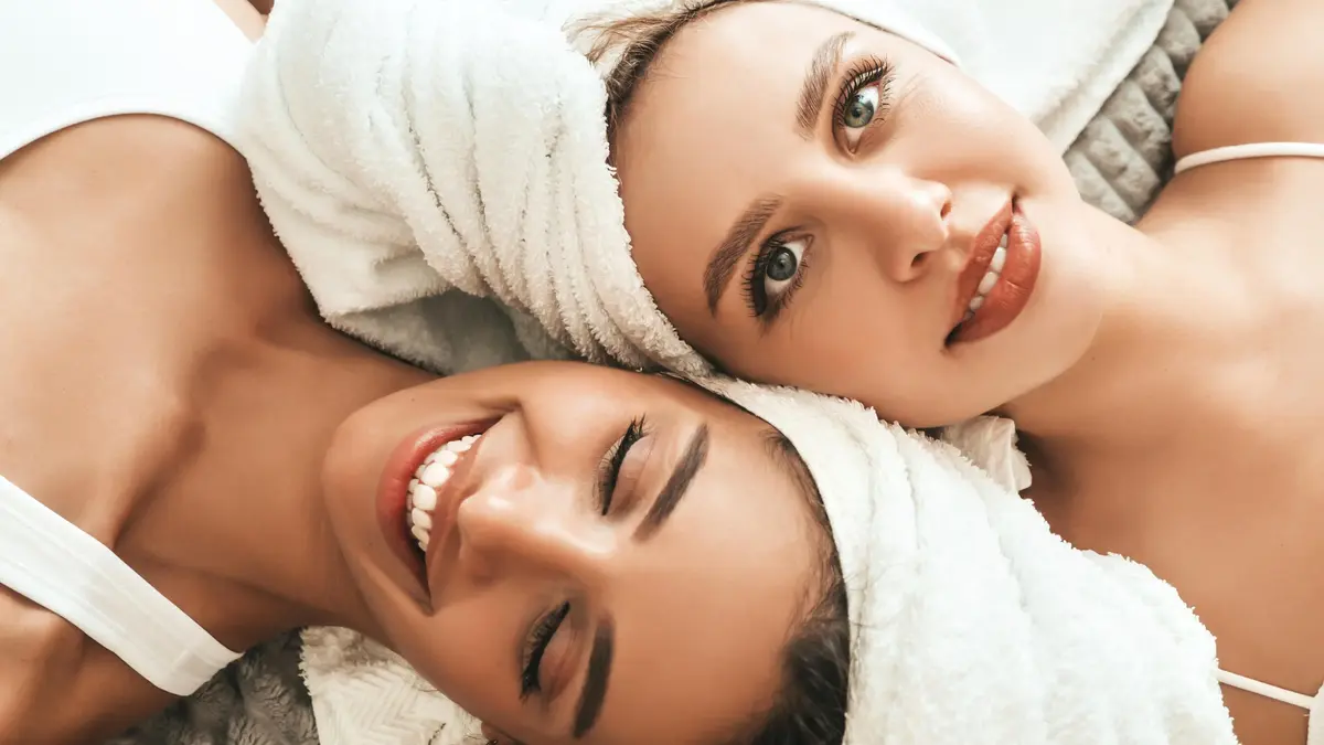 Two young beautiful smiling women white bathrobes towels head