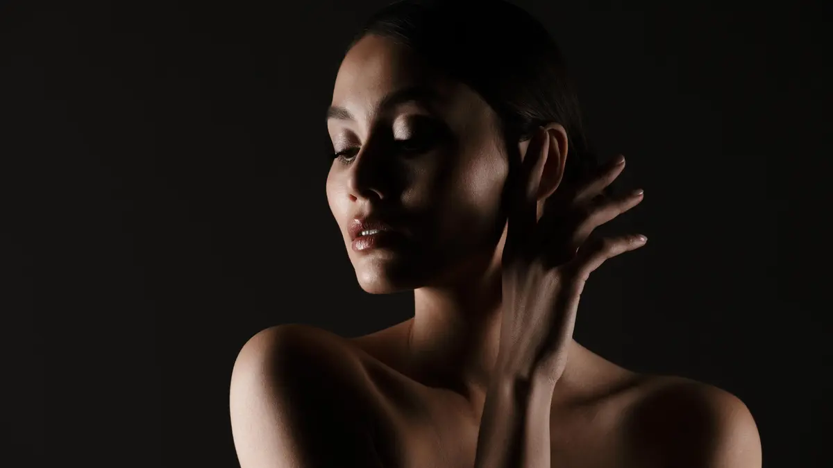 Portrait feminine tender woman with sensual look looking aside low lights isolated black