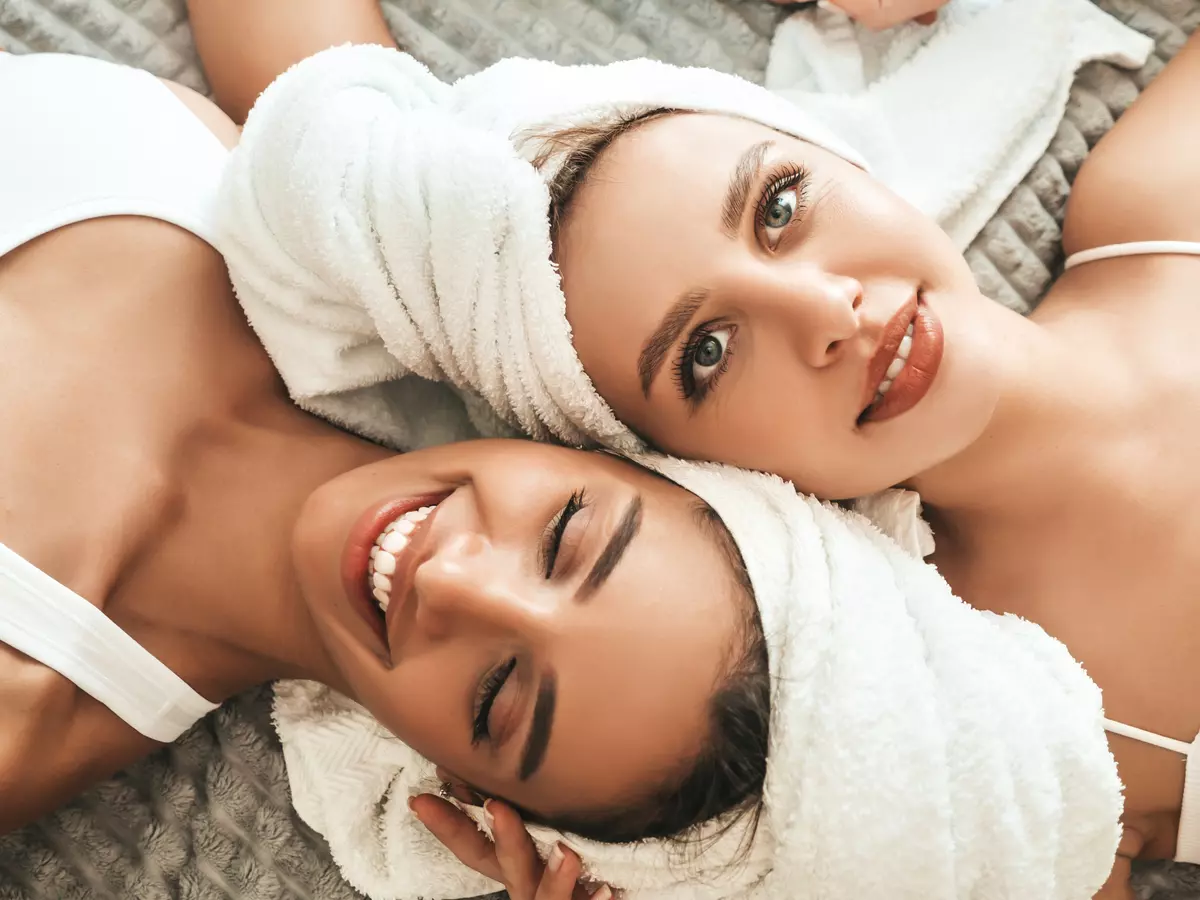 Two young beautiful smiling women white bathrobes towels head