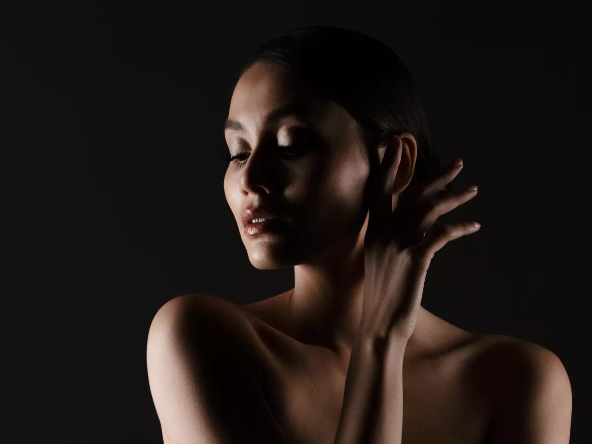 Portrait feminine tender woman with sensual look looking aside low lights isolated black