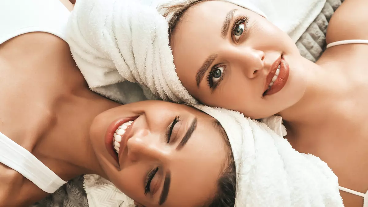 Two young beautiful smiling women white bathrobes towels head