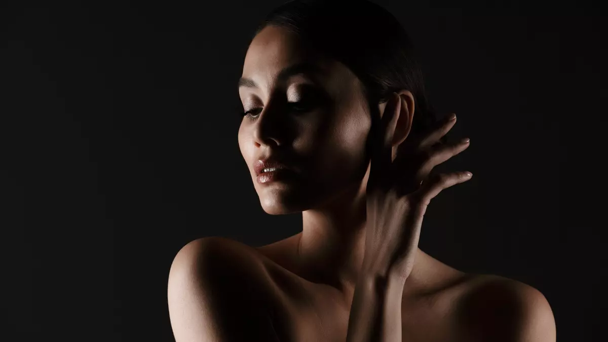 Portrait feminine tender woman with sensual look looking aside low lights isolated black